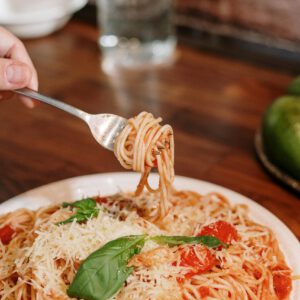 Close-up of a hand twirling spaghetti with tomato sauce and basil, perfect Italian meal.