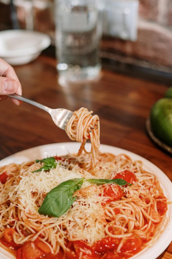 Close-up of a hand twirling spaghetti with tomato sauce and basil, perfect Italian meal.