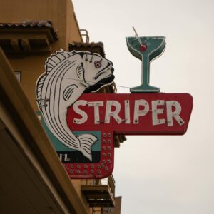 Colorful vintage sign featuring a fish and cocktail glass on an urban street.