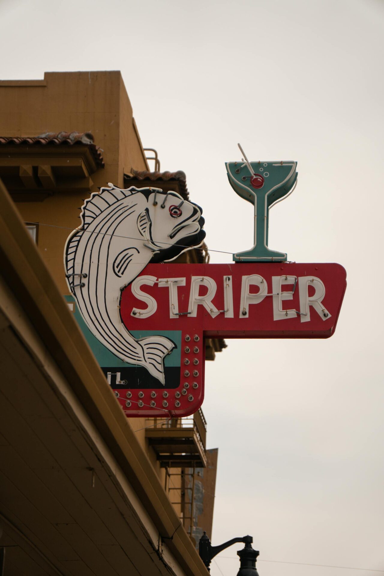 Colorful vintage sign featuring a fish and cocktail glass on an urban street.